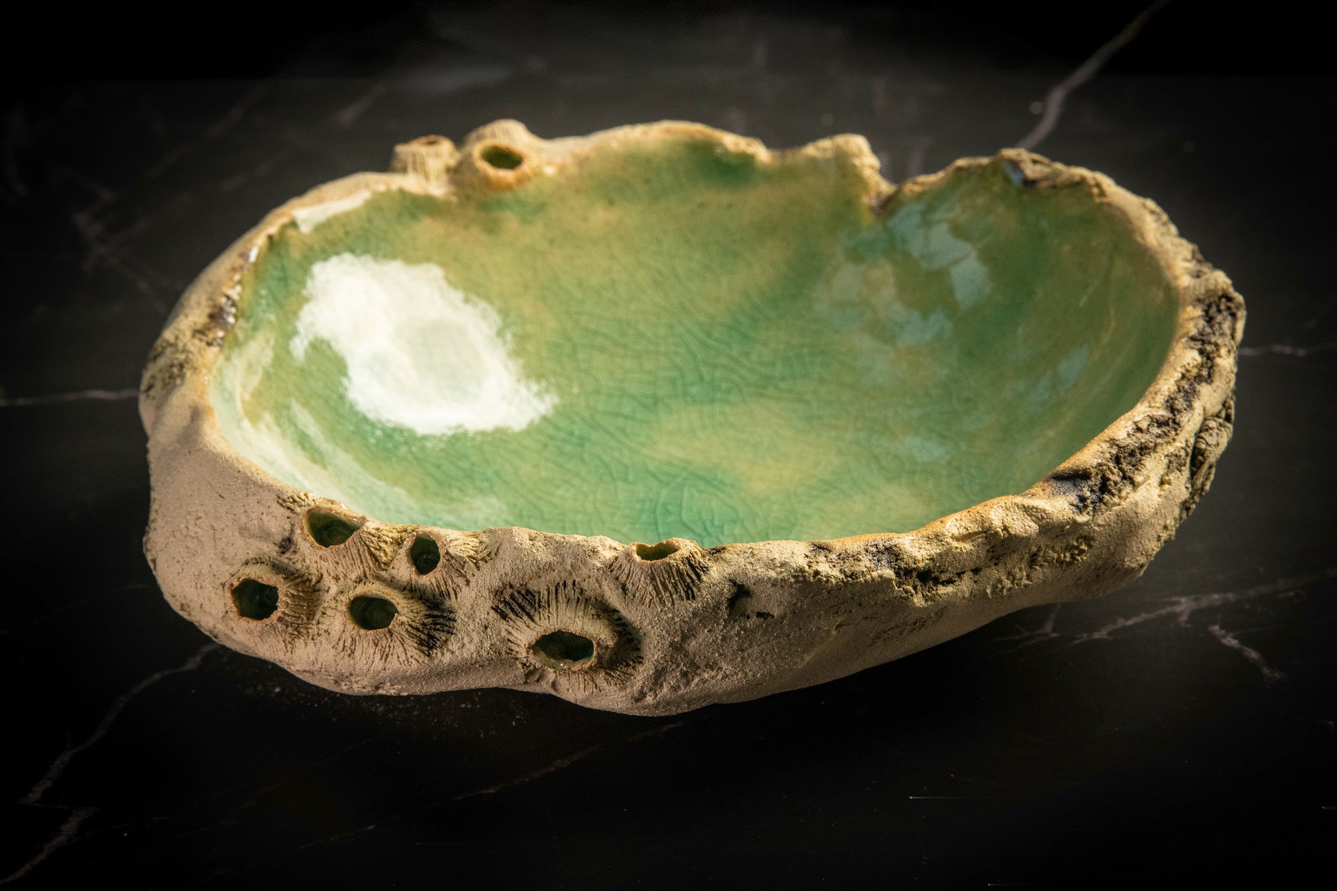 Ceramic bowl with textured surface and green glaze on a black background